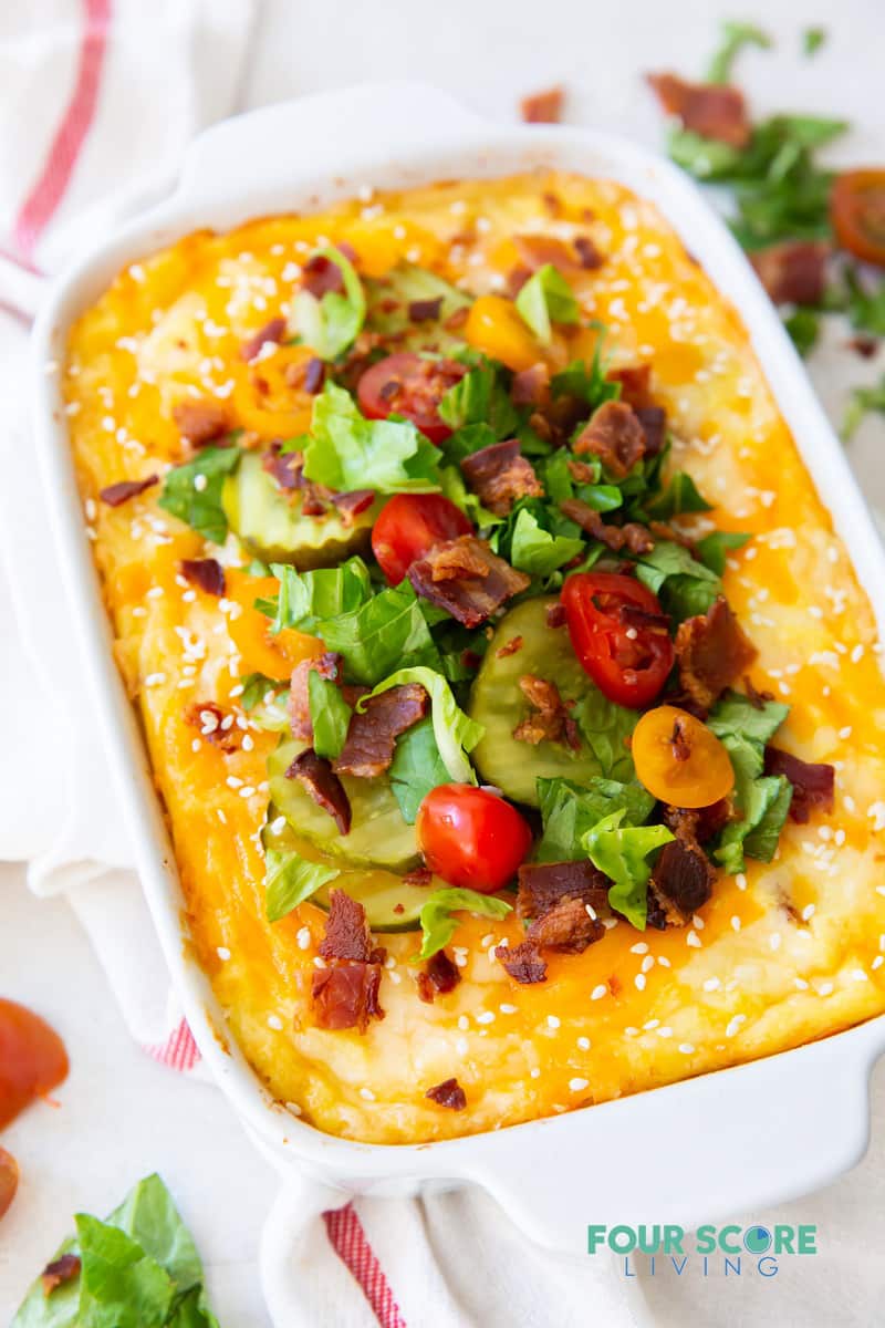 a rectangular casserole dish of cheeseburger casserole topped with lettuce, pickles, tomato, and bacon