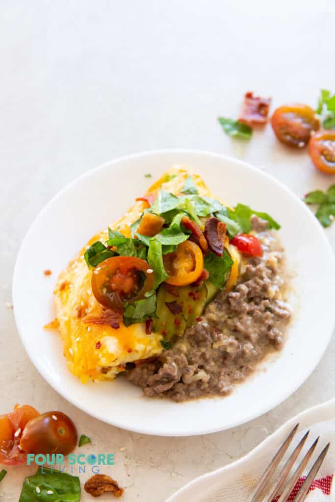 a round plate with one serving of cheeseburger casserole topped with tomato, lettuce, pickles, and bacon