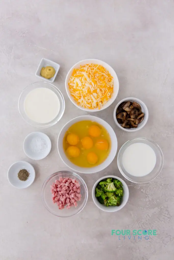 all of the ingredients for quiche in separate bowls, including eggs, cheese, cream, and fillings.