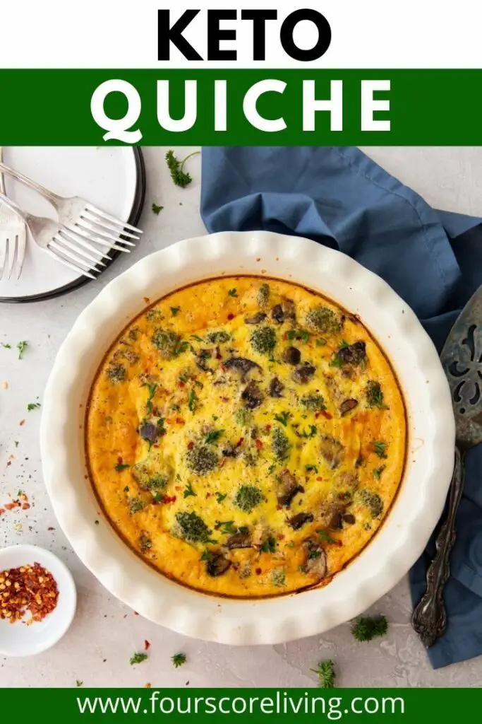 top down view of a quiche in a white ceramic pie pan next to a white plate with three forks, a pie server, and a blue napkin.