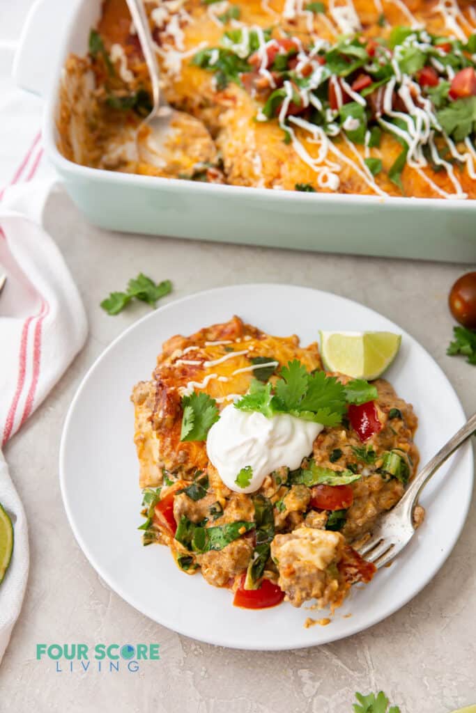 a plate of keto taco casserole topped with sour cream and cilantro, next to a casserole dish full of the same.