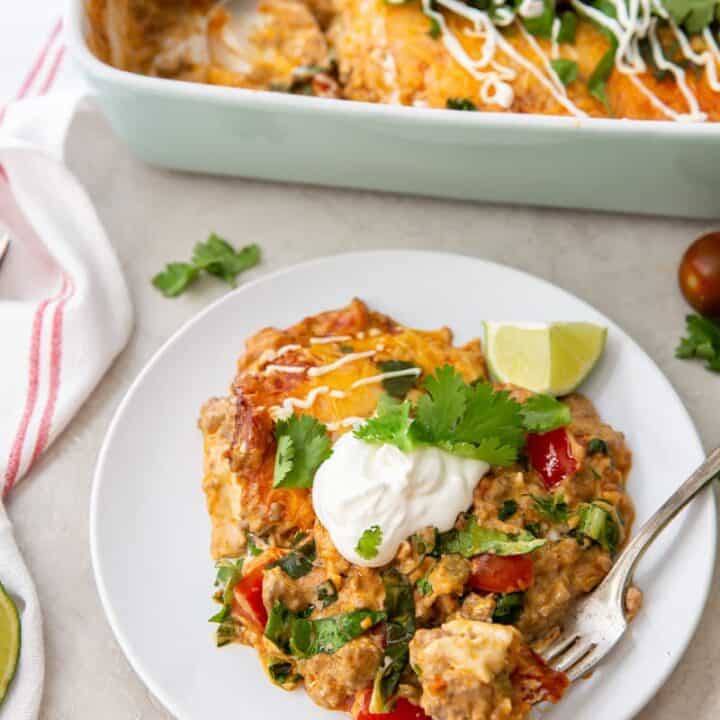 a plate of keto taco casserole topped with sour cream and cilantro, next to a casserole dish full of the same.