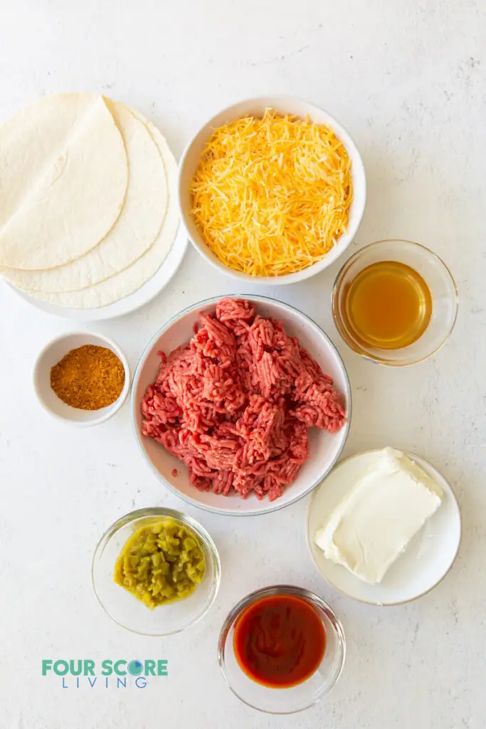 all of the ingredients for keto taco casserole, each in separate bowls, including ground meat, tortillas, cheese, and seasonings.