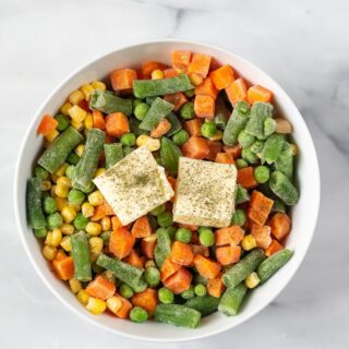 frozen mixed vegetables in a white bowl with butter on top