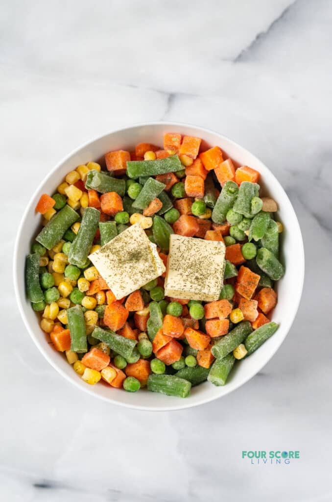 frozen mixed vegetables in a white bowl with butter on top