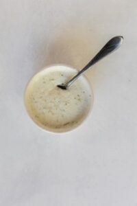 Top view photo of a bowl filled with ranch seasoning, garlic, salt, and pepper, and cream, mixed together with a silver spoon.