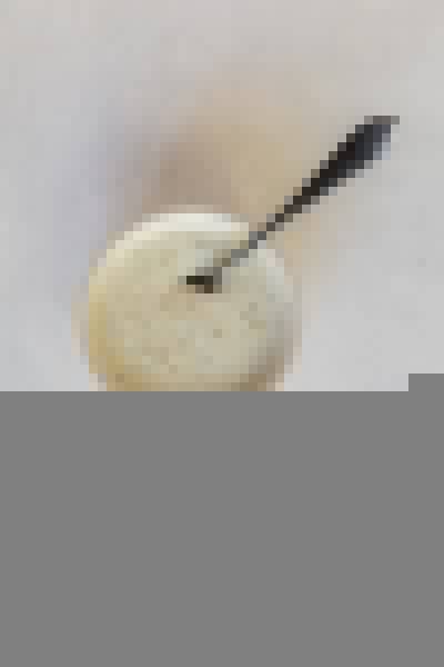 Top view photo of a bowl filled with ranch seasoning, garlic, salt, and pepper, and cream, mixed together with a silver spoon.
