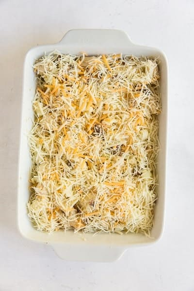 Top view photo of the Keto Chicken Bacon Ranch mixture in a casserole pan and topped with cheese, ready to bake.