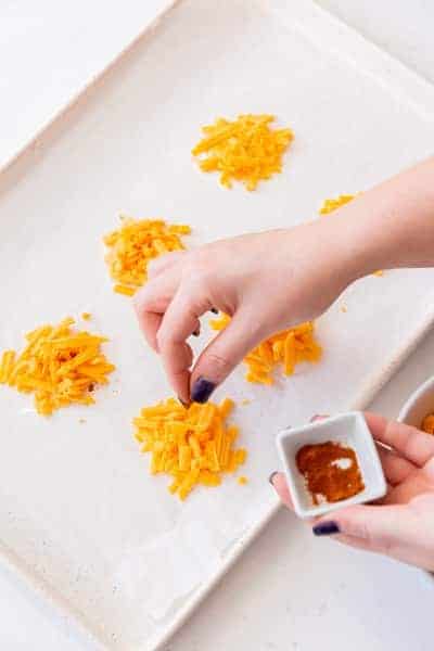 Photo of a hand sprinkling seasoning on multiple cheese stacks on the baking sheet.