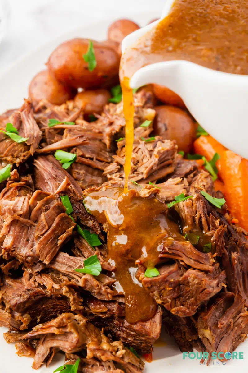 a plate of tender pot roast with gravy being poured on.