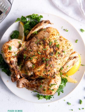 a whole chicken seasoned with herbs and lemon on a round white platter next to an instant pot.