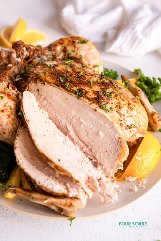 closeup view of a sliced breast from a roasted whole chicken. the plate is garnished with lemon slices and parsley