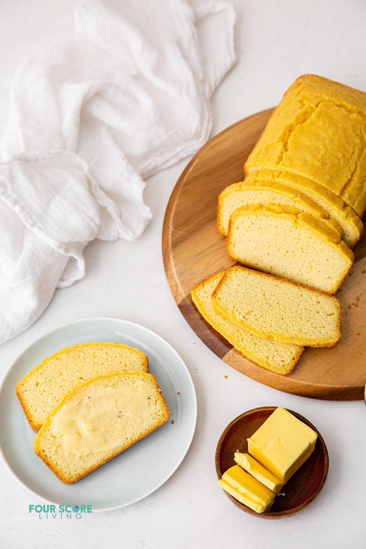 a round wooden board with a load of keto bread, sliced. There's a plate with two pices of bread spread with butter and a small plate with yellow butter