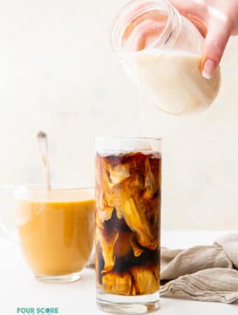 a tall glass of iced coffee with homemade keto creamer being poured in from a mason jar. A clear glass of hot coffee with cream is in the background