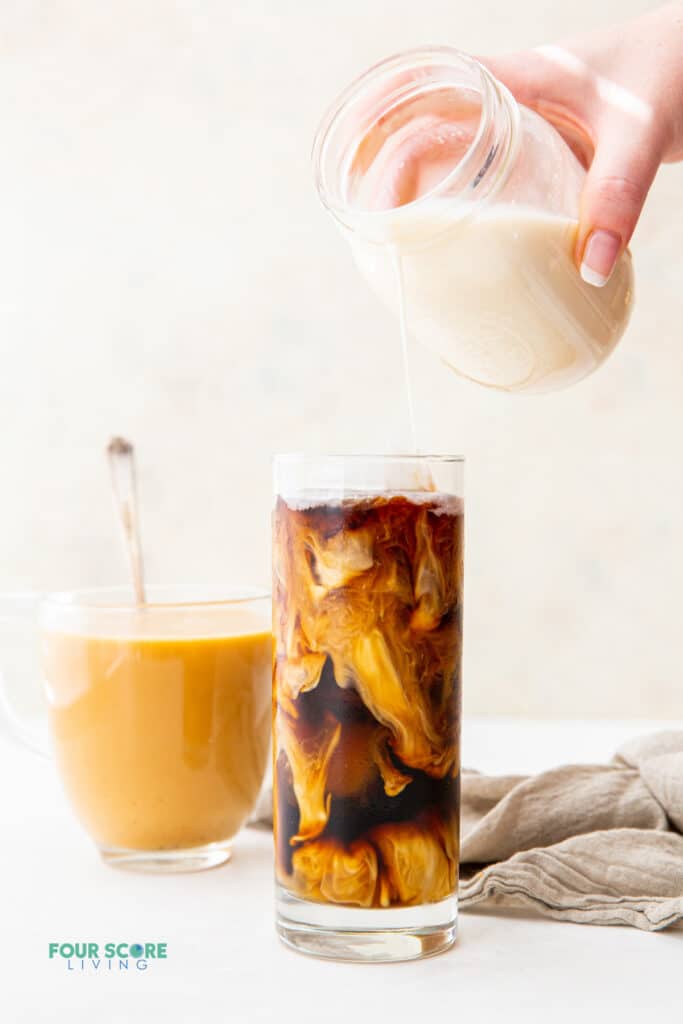 a tall glass of iced coffee with homemade keto creamer being poured in from a mason jar. A clear glass of hot coffee with cream is in the background