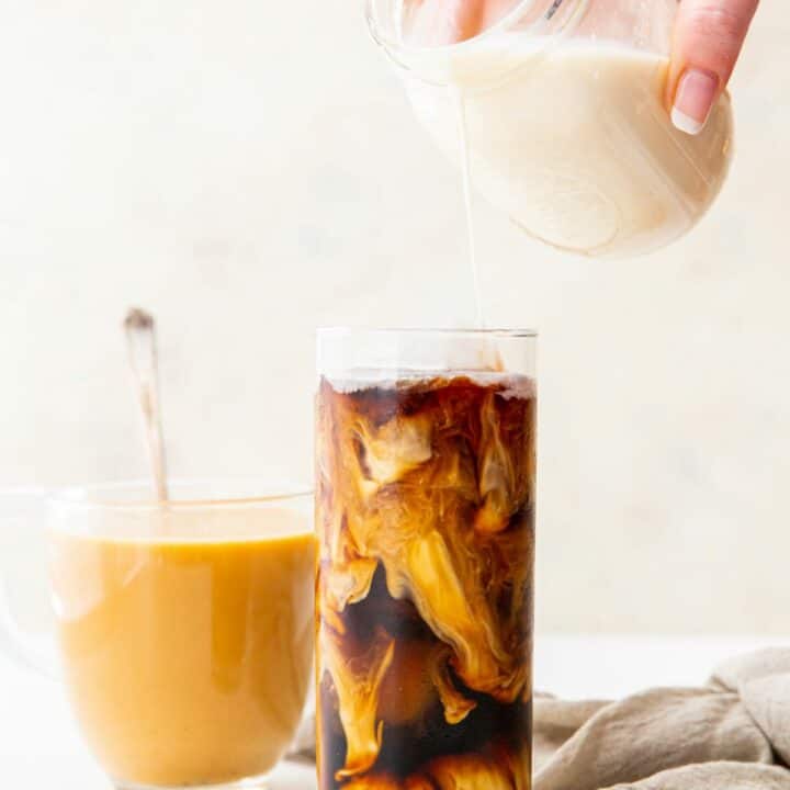 a tall glass of iced coffee with homemade keto creamer being poured in from a mason jar. A clear glass of hot coffee with cream is in the background
