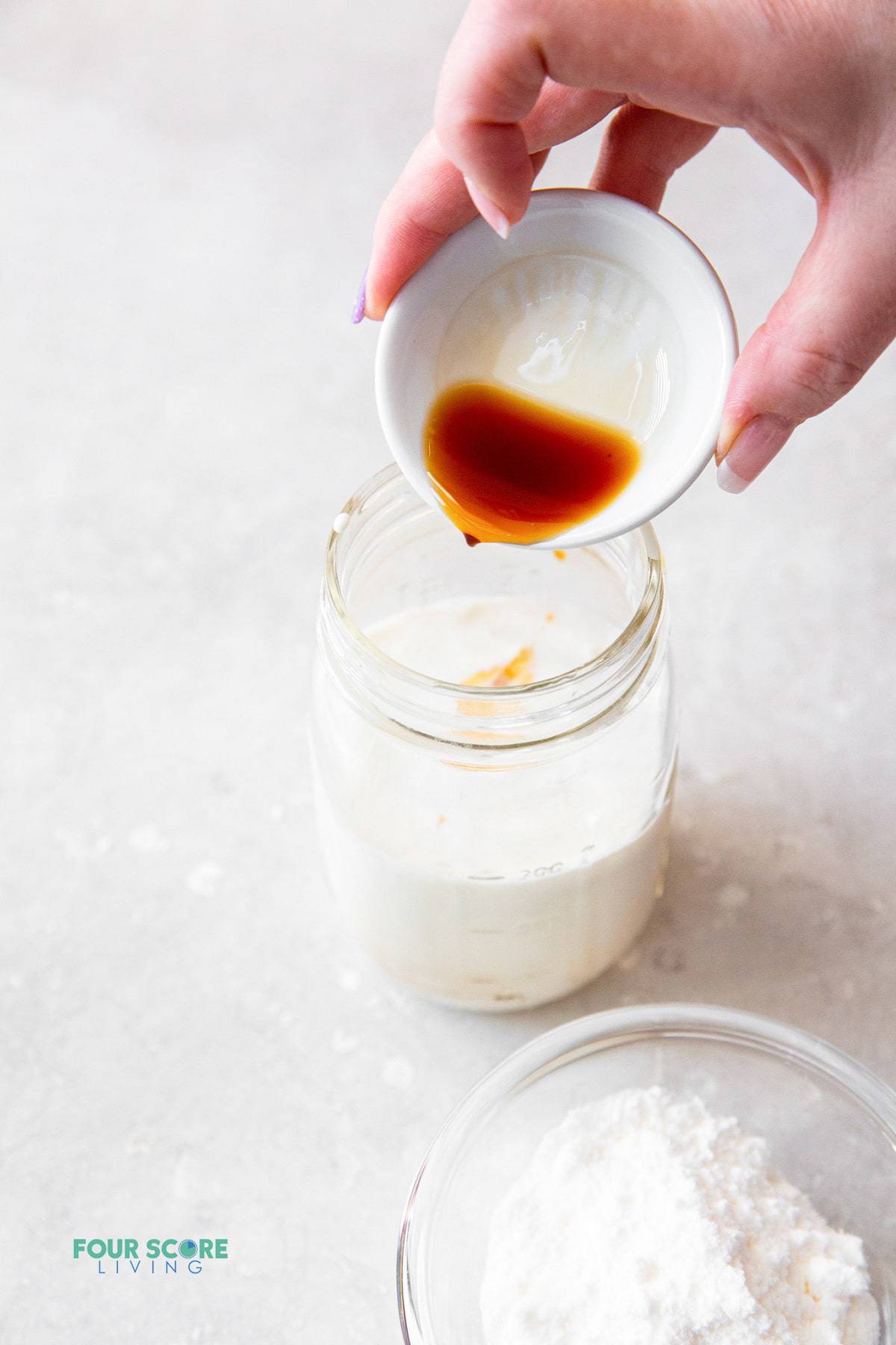 image showing a woman pouring vanilla extract into a mason jar filled with heavy cream and almond milk