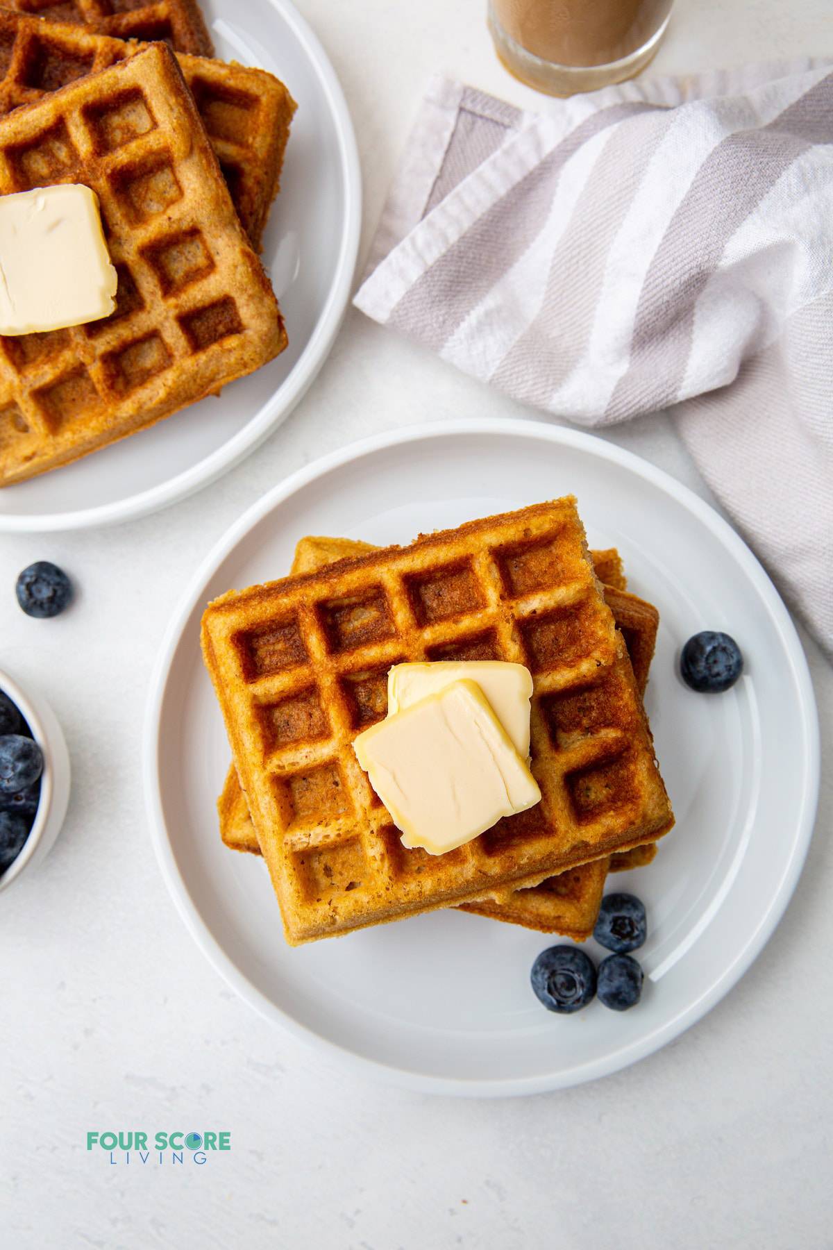 two plates with keto waffles topped with pats of butter and with blueberries on the side