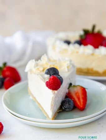 a slice of no-bake cheesecake with the point facing you on a pale green doubled plate. The slice is topped with fresh berries and whipped cream