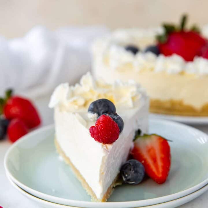 a slice of no-bake cheesecake with the point facing you on a pale green doubled plate. The slice is topped with fresh berries and whipped cream