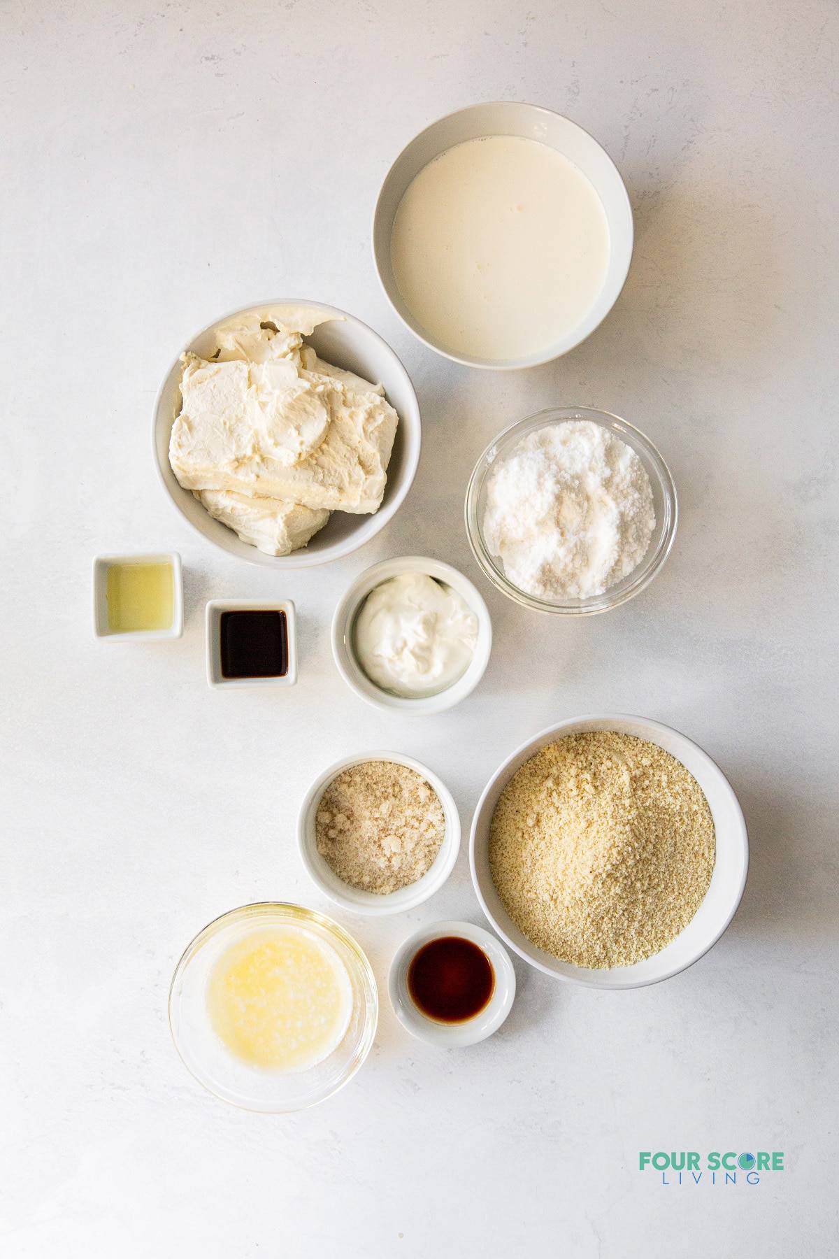 The ingredients for keto no bake cheesecake all in separate small bowls on a marble countertop.