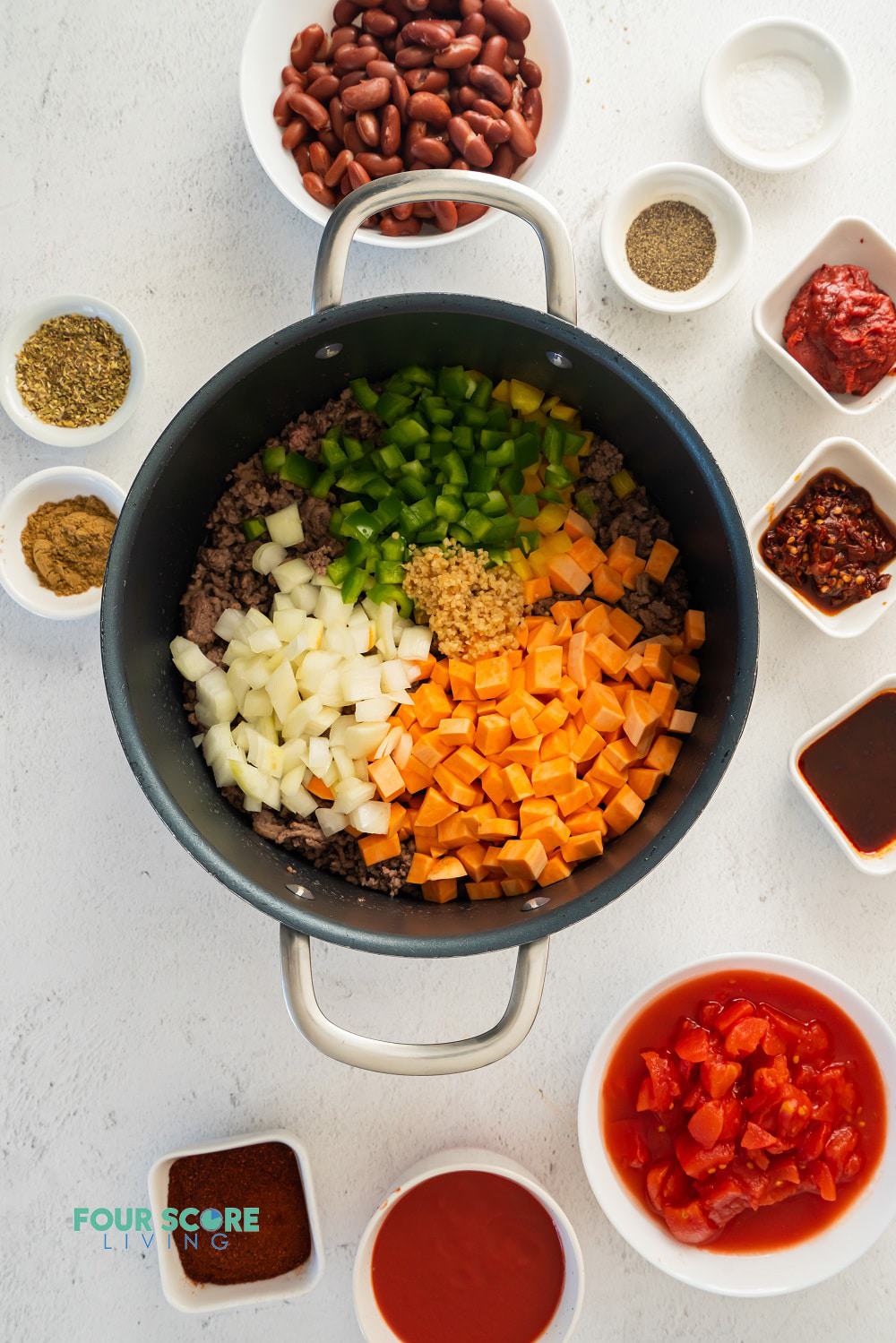 The ingredients for chipotle chili, with meat and vegetables in a pot and seasonings in small bowls surrounding it.