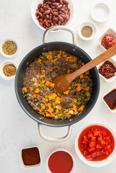 Top view photo of a large stockpot filled with browned ground beef, sweet potato, onion, bell pepper, and garlic, and cooked until vegetables are softened.