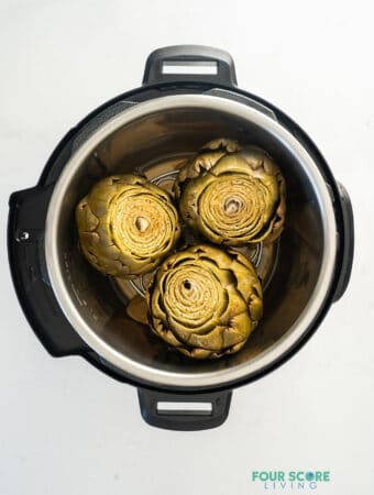 View from above of an instant pot, opened, with three cooked artichokes inside.