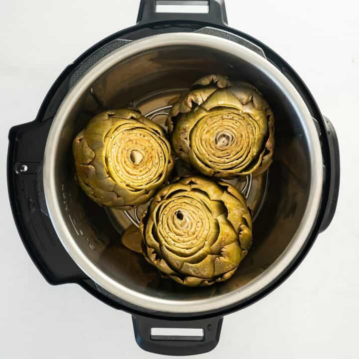View from above of an instant pot, opened, with three cooked artichokes inside.
