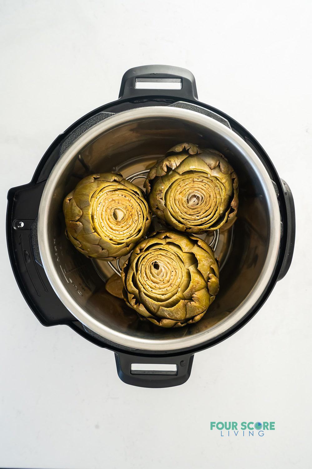 View from above of an instant pot, opened, with three cooked artichokes inside.