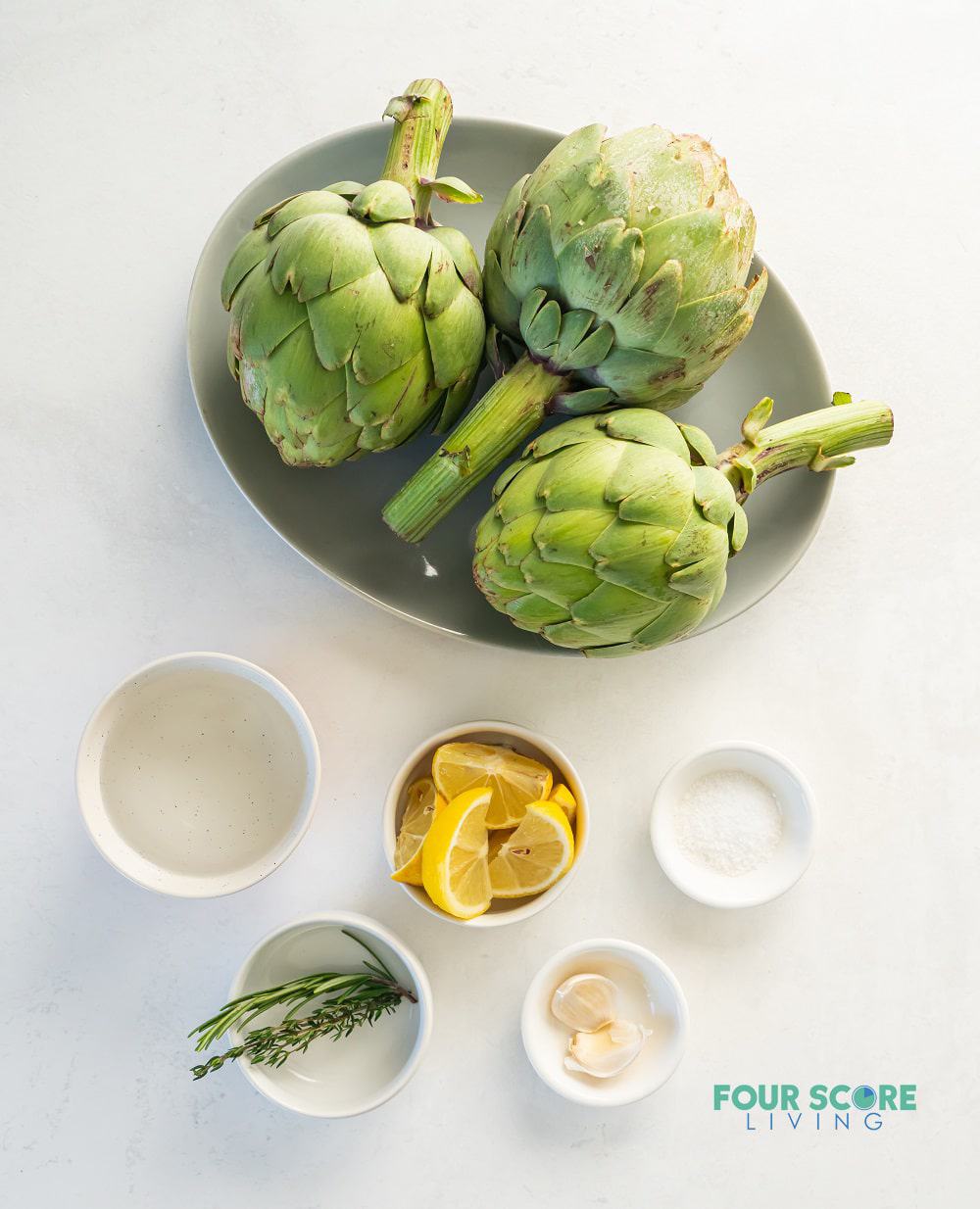 The ingredients needed to make instant pot artichokes, including three artichokes, lemon, garlic, and seasonings.
