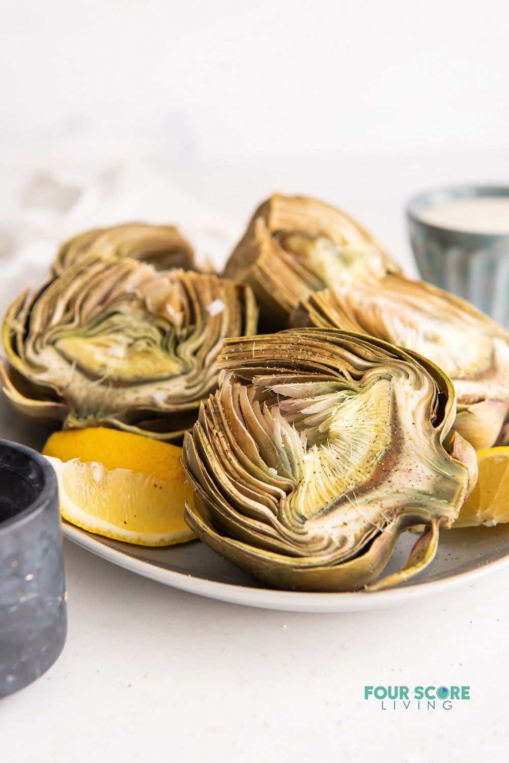 a plate of halved artichokes garnished with lemon wedges.