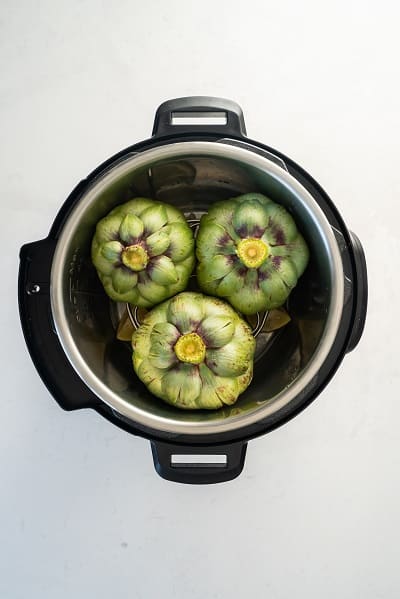 Top view photo of 3 artichokes inside the Instant Pot, cut-side down, and ready to cook.