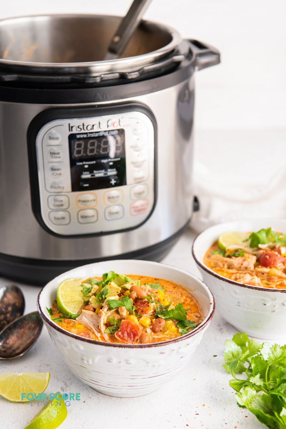Two bowls of white chicken chili with lime, and cilantro garnishes in front of an Instant Pot.