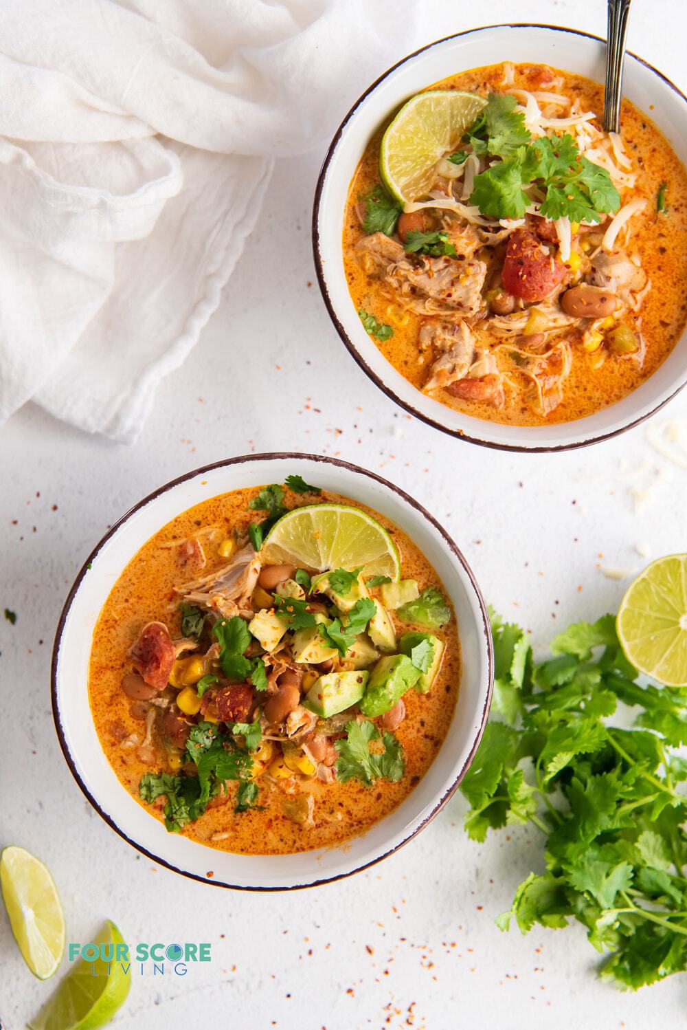 Two bowls of white chicken chili with lime, and cilantro garnishes, viewed from above