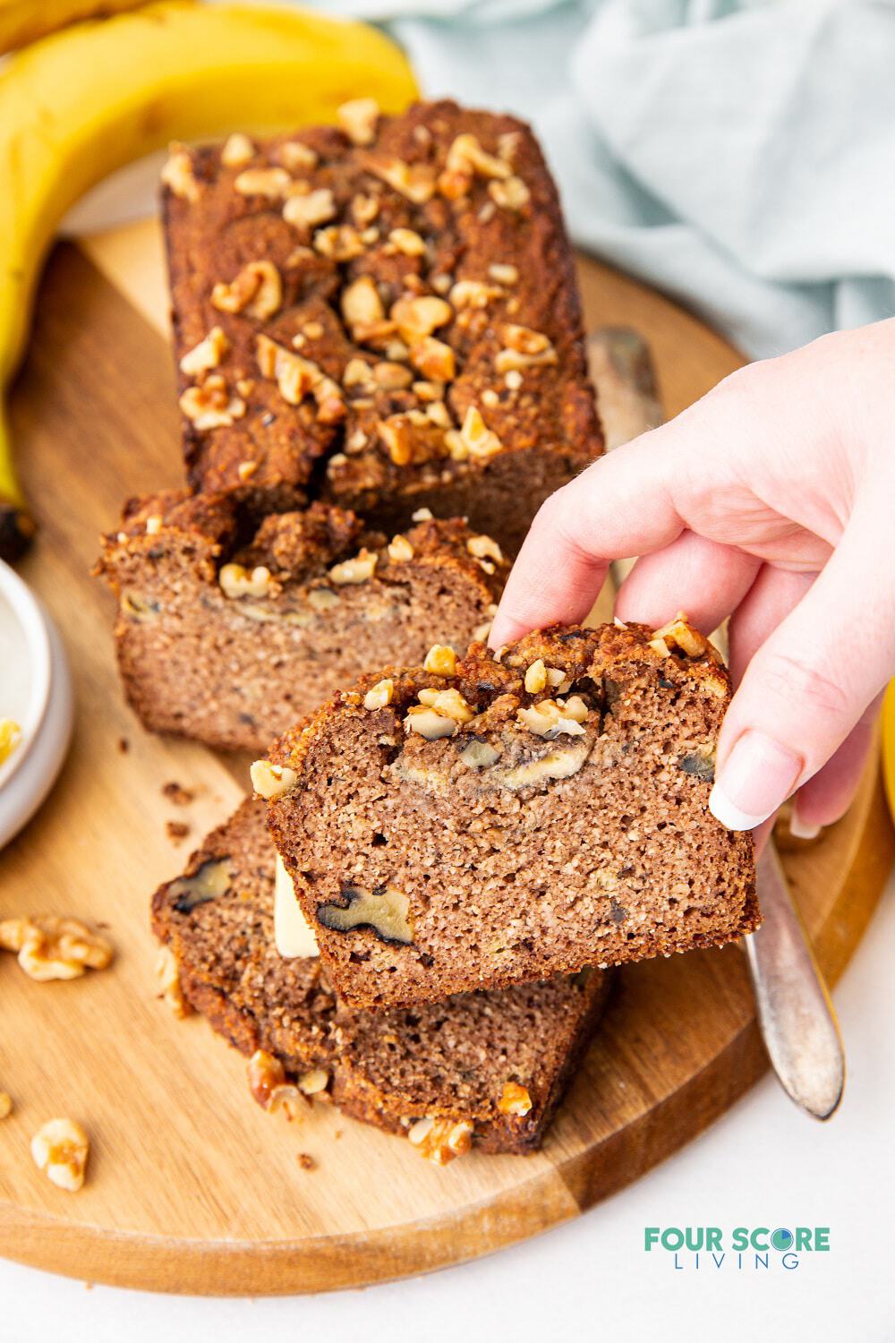a hand holding a slice of banana bread to show the nuts and texture inside.