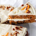 A wedge slice of two layer keto carrot cake being removed from the whole cake. Carrot cake is topped with frosting, chopped walnuts and carrot curls.