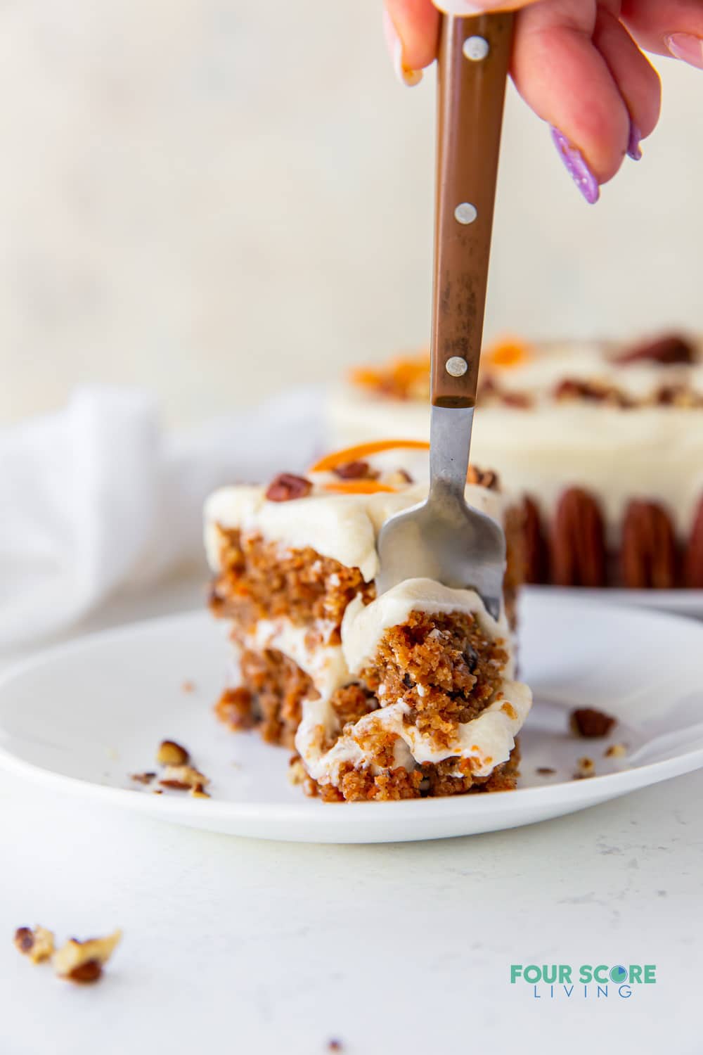 a woman's hand with a fork is taking a bit of carrot cake with cream cheese frosting.