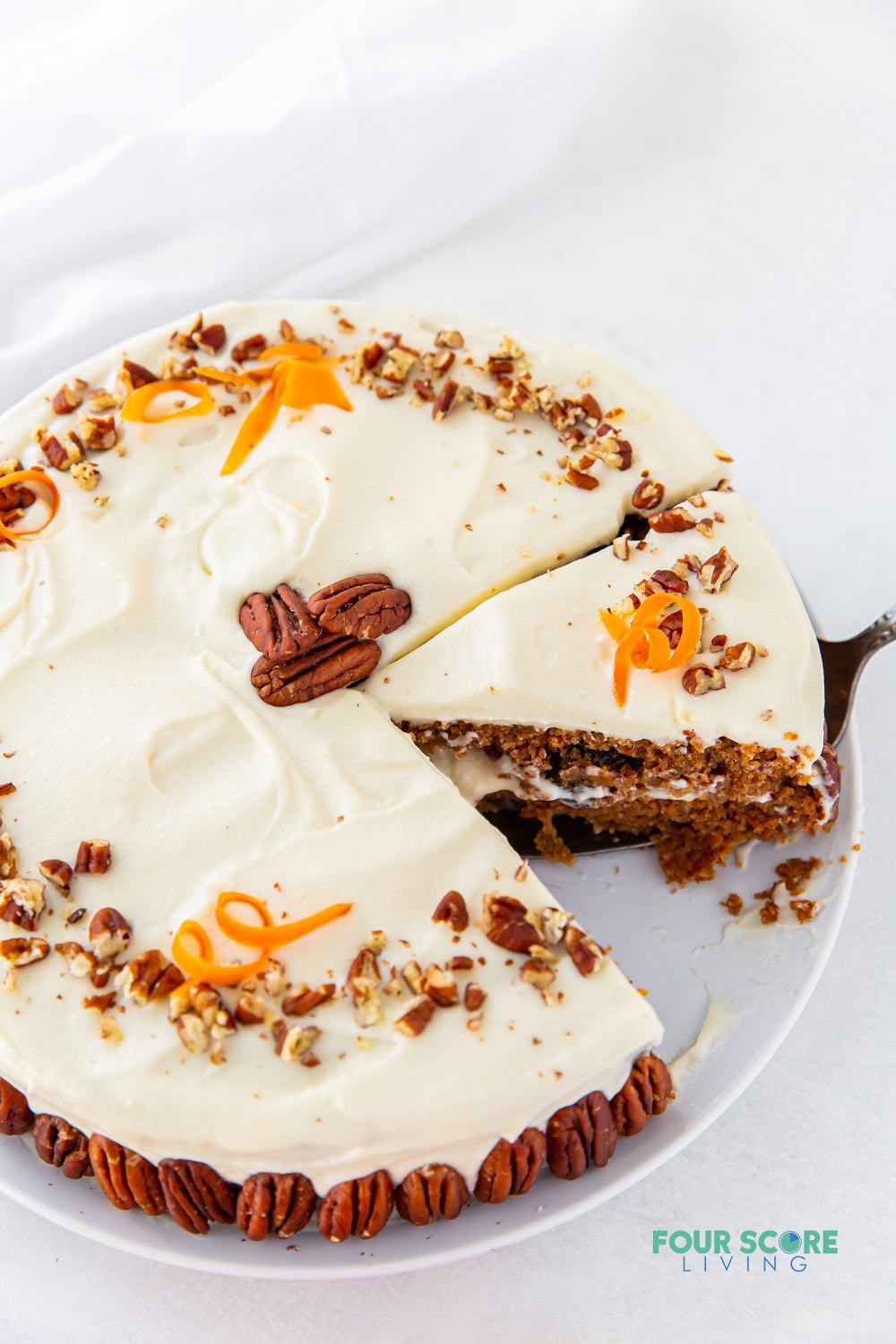 a round carrot cake decorated with whole pecans, chopped pecans. One slice is missing and a second is being served.