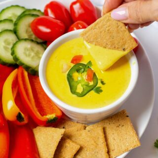 hand holding a cracker dipped into keto queso