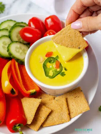 hand holding a cracker dipped into keto queso