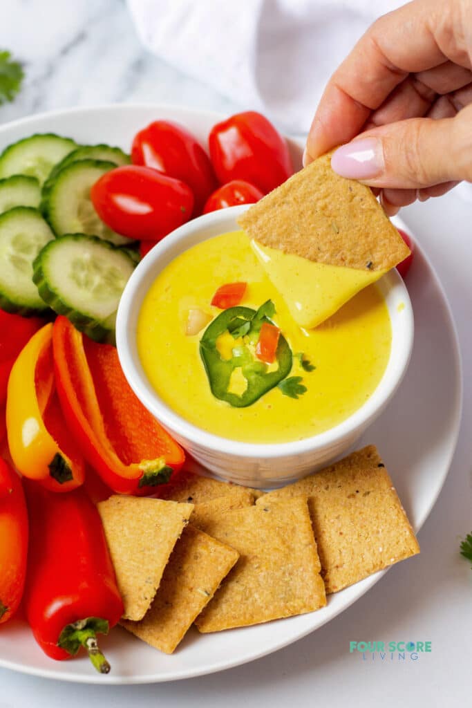hand holding a cracker dipped into keto queso