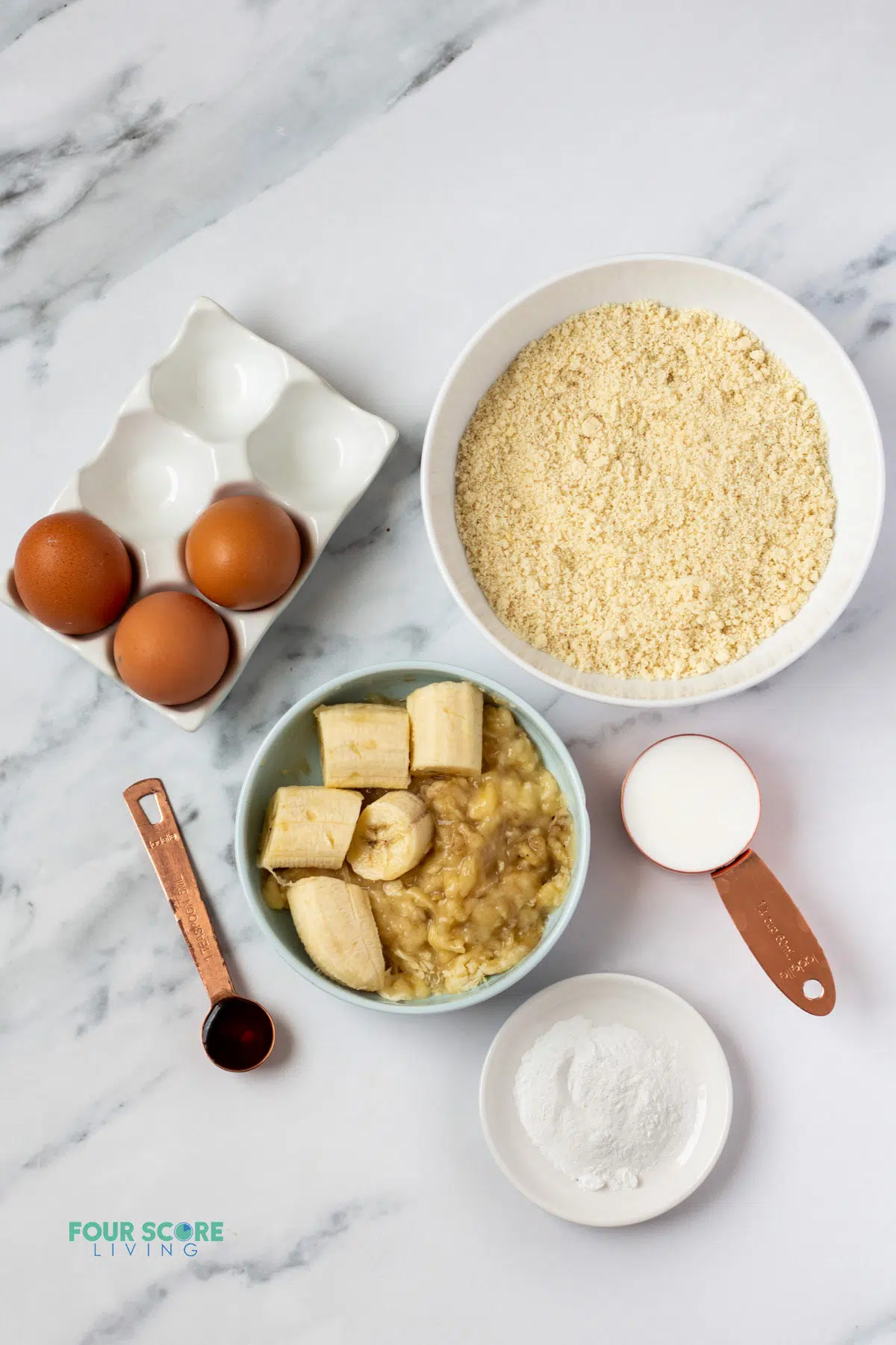 The ingredients needed to make almond flour banana pancakes, measured into separate bowls on a marble counter.