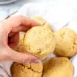 a feminine hand holding a round biscuit above a basket of biscuits.