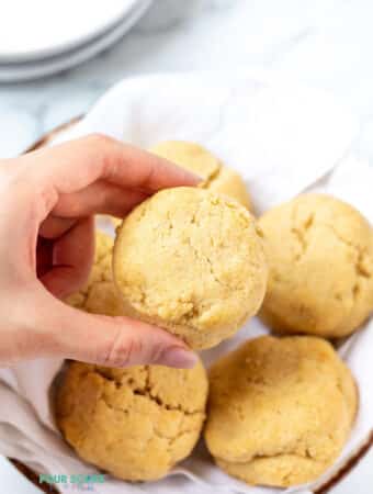 a feminine hand holding a round biscuit above a basket of biscuits.