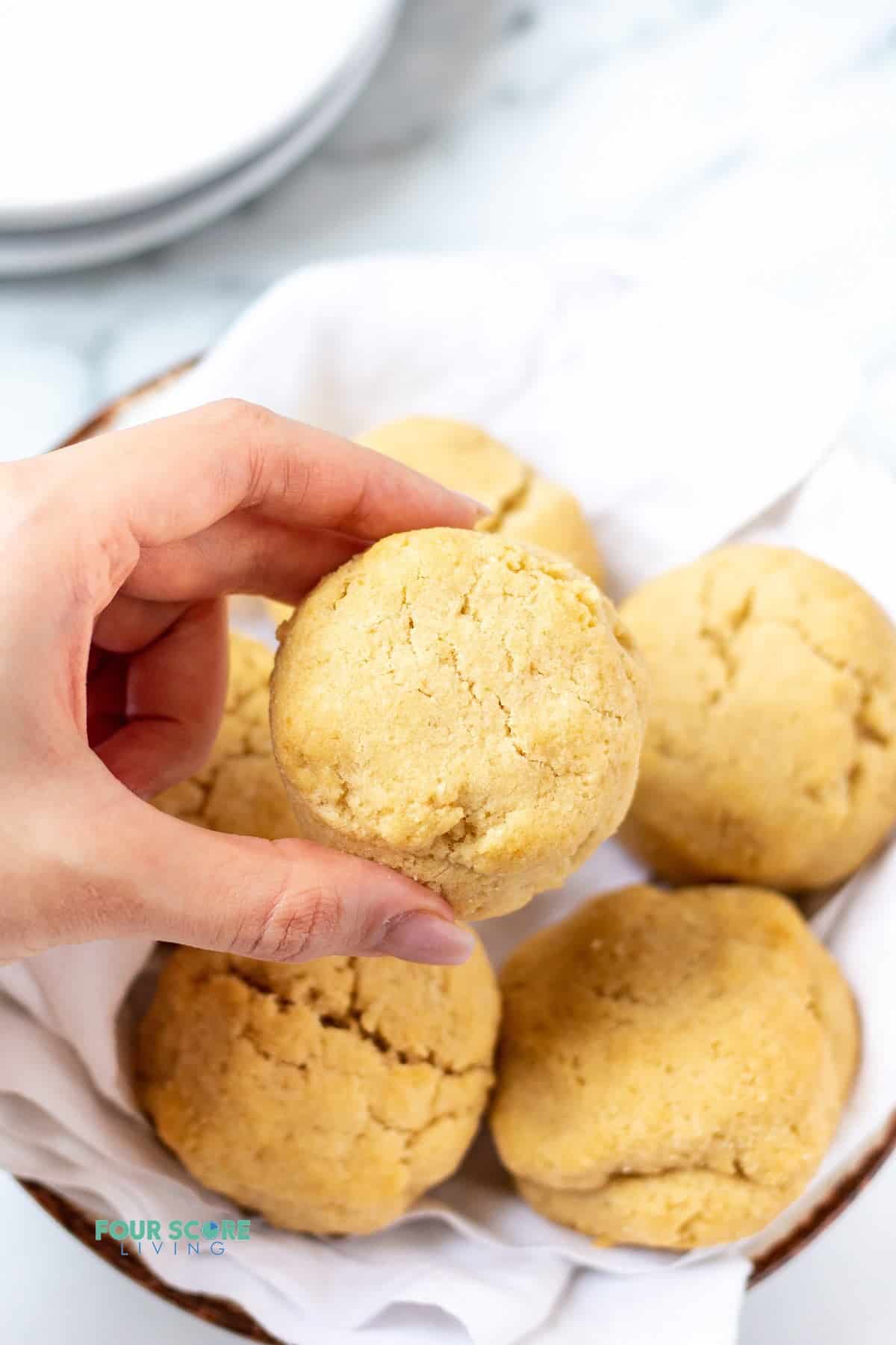 a feminine hand holding a round biscuit above a basket of biscuits.