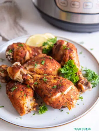 a plate of cooked chicken legs in front of an instant pot.
