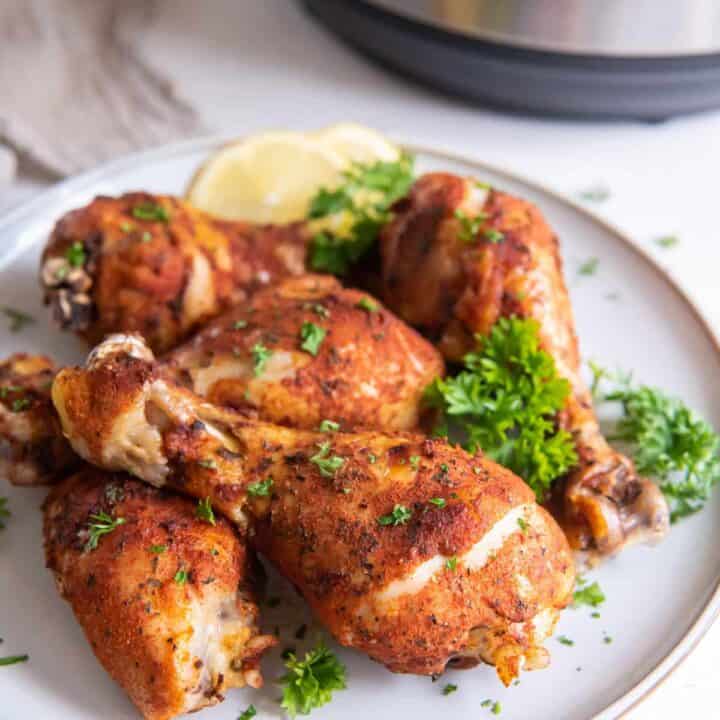 a plate of cooked chicken legs in front of an instant pot.