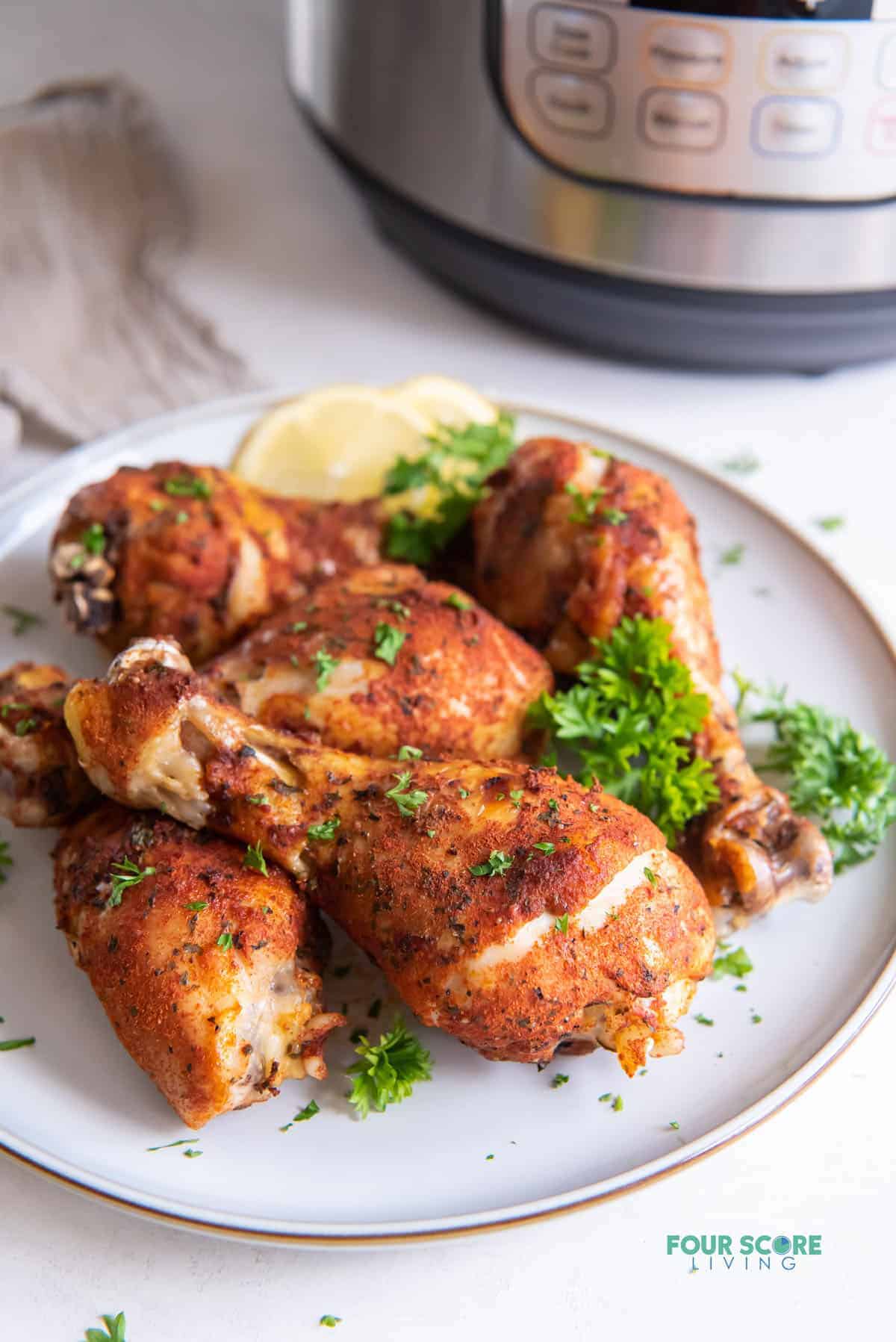 a plate of cooked chicken legs in front of an instant pot.