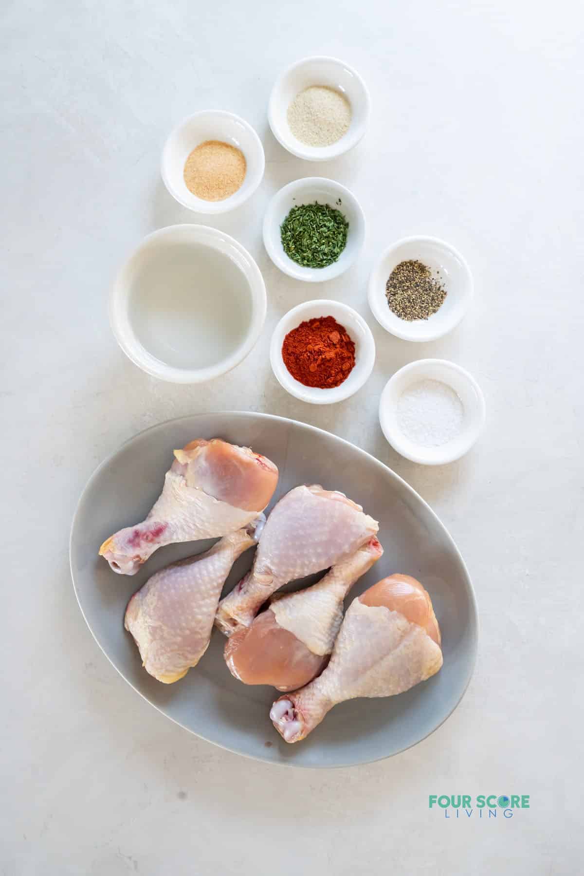 an oval plate of raw chicken legs next to the seasonings needed to make them in the instant pot.